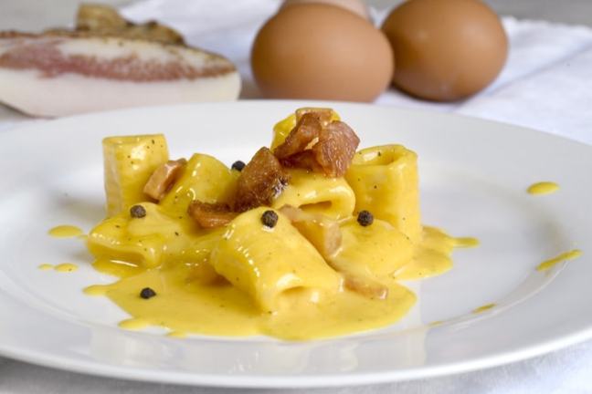 Plate of pasta carbonara with pancetta and creamy yellow sauce.