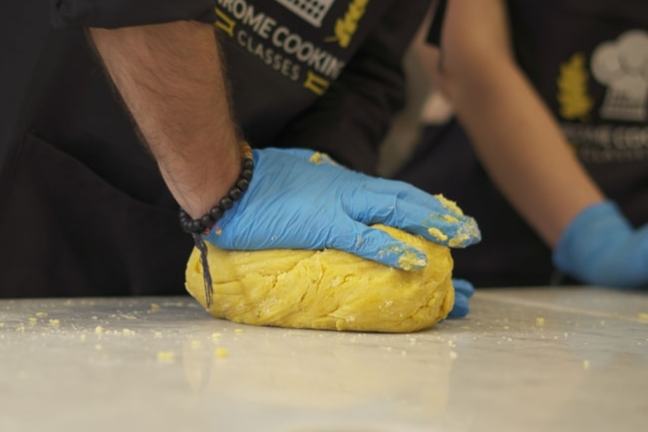 Person with blue gloves kneading yellow dough on a table.
