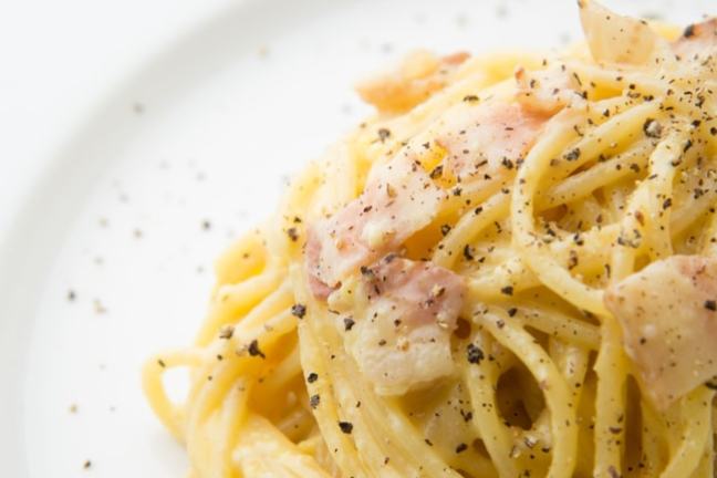 Plate of spaghetti carbonara with bacon and black pepper.