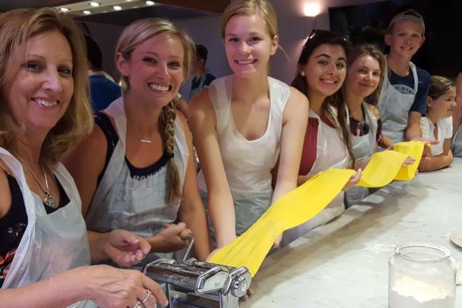 Group of people making pasta using a pasta machine at a kitchen counter.