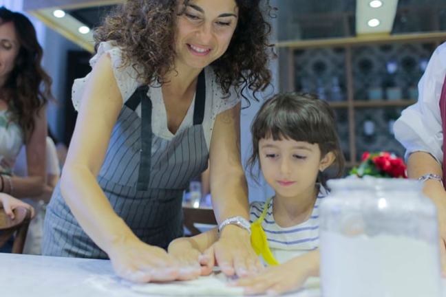 Woman and child kneading dough together in a kitchen setting.